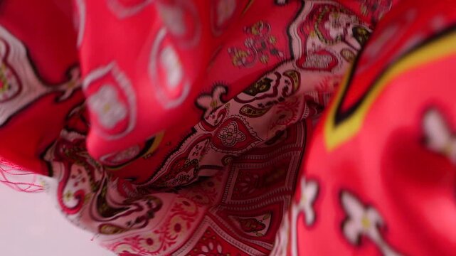 Pink silk scarf falls onto a white background. This elegant textile showcases smooth texture and floral oriental patterns. Fluid movement is ideal for commercial fashion advertisements.