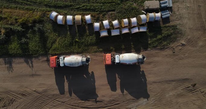Top-down aerial view of two concrete mixer trucks parked next to large wooden cable spools on a dirt construction site