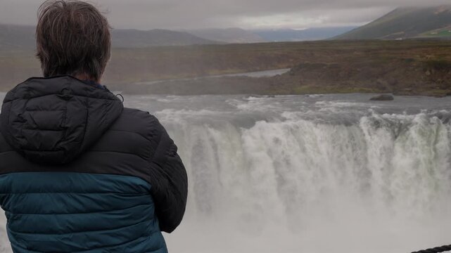 Solitary mature man admiring the powerful and scenic Godafoss waterfall in Iceland. Tourist enjoying the stunning nordic natural landscape