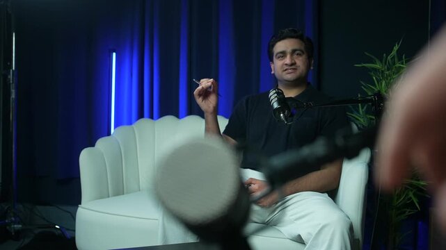 Podcast guest talking in modern studio with blue ambient lighting, medium talking as microphone opposite is moved into position
