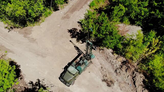 Aerial drone view of a mobile geotechnical drilling rig conducting soil investigation and ground sampling at a future construction site near a forested area in Sumy, Ukraine. The specialized drilling 