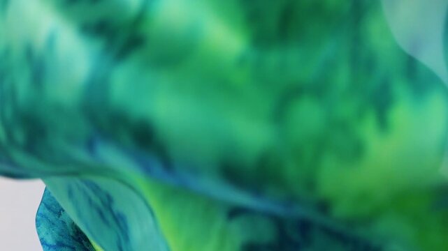 Natural silk fabric falls onto a white background. Emerald and blue tie-dye patterns reveal luxurious texture. Fluid movements of soft material create a perfect template for premium textile production