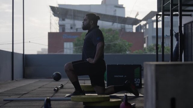 Bearded male athlete performing a kneeling hip flexor stretch during a mobility training session in a modern indoor fitness studio.