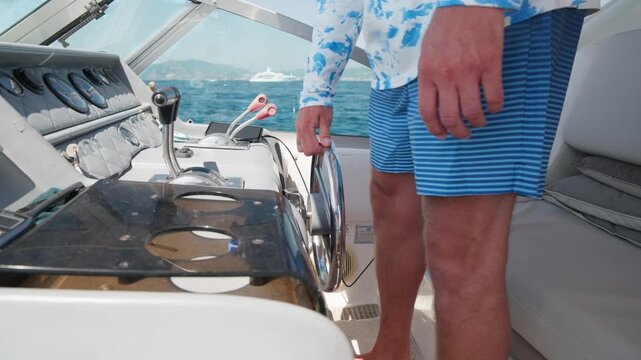 Young skipper enjoying a sunny day, navigating a motorboat with his hand on the steering wheel while enjoying a beautiful view of the coastline and the blue sea during a summer vacation