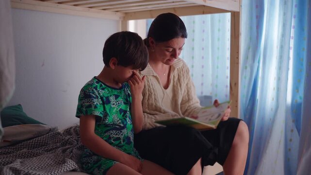 Mother helping son learn to read before bedtime while sharing storybook together creating nurturing family moment focused on education literacy and parental support