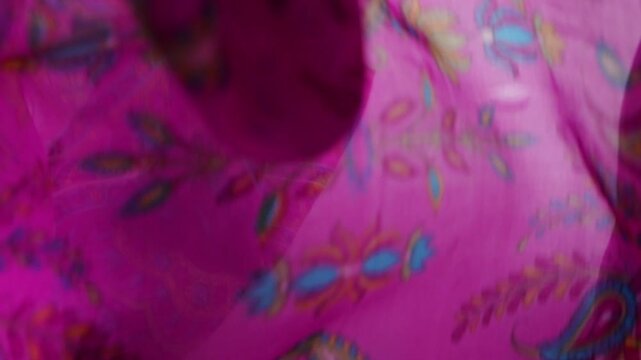 Fuchsia silk fabric with paisley patterns drops onto a white background. This elegant motion showcases luxury textile texture. Pink and purple colors are ideal for fashion and apparel advertising.