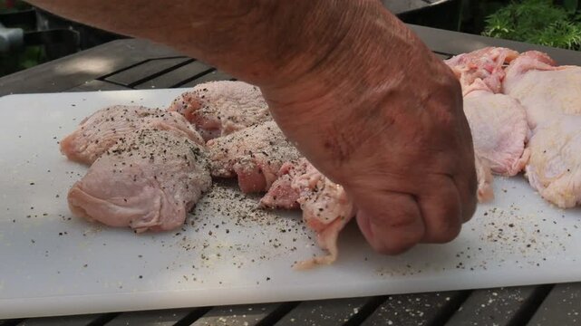 Close-up of raw chicken thighs being prepared for a backyard BBQ with herbs and spices on a cutting board
