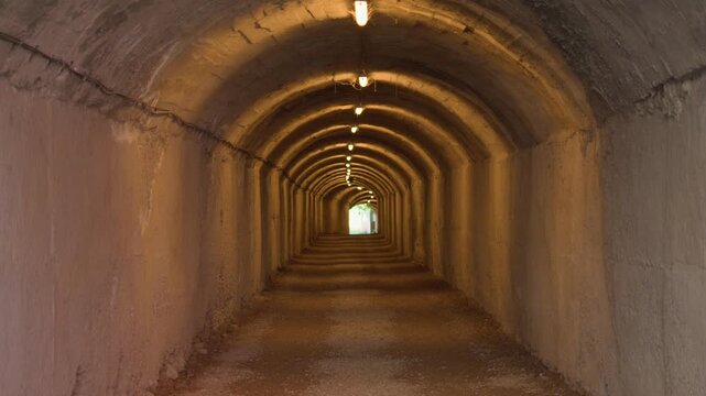 A symmetric perspective view of a lit concrete tunnel path leading toward a bright outdoor exit.