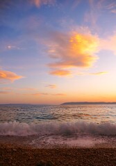 Fototapeta premium Waves on the wind with foam on the sea horizon with colorful clouds in sunset summer sunset background