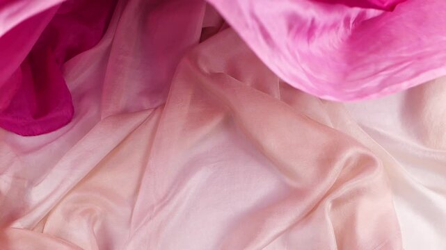 Pink silk fabric falls smoothly onto bright textiles. Soft flowing material creates elegant waves. Moving background serves as a perfect backdrop for fashion and luxury brand cosmetic videos.