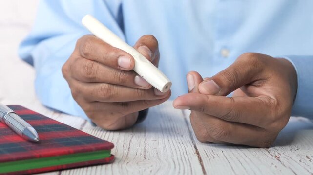 A man in a blue shirt performs a finger prick test to check his blood glucose level using a lancet, capturing the dynamic motion of this medical procedure