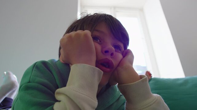 Young boy lying on sofa completely absorbed in off screen entertainment, modern childhood scene highlighting screen time, digital media consumption, immersion and focused attention