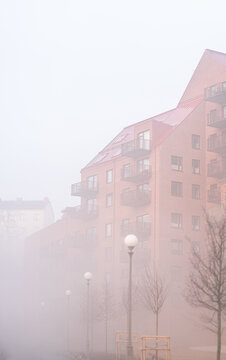 Urban brick apartment complex partially hidden in thick atmospheric morning fog.
