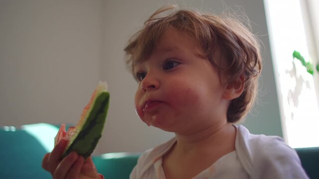 Happy toddler eating watermelon slice during relaxed moment at home, wholesome childhood image focused on nutrition, healthy habits and joyful everyday living