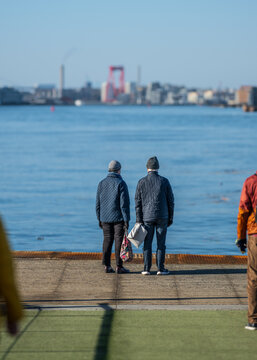 Two people standing by waterfront looking across harbor city skyline.
