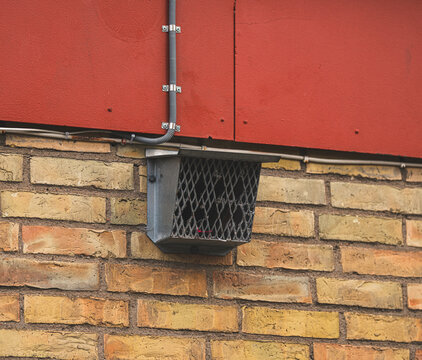 Metal wall vent mounted on brick facade with utility conduit.