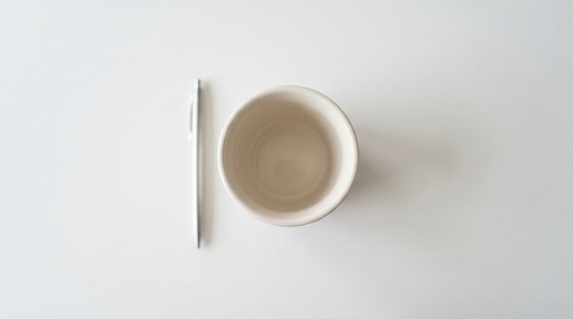 Minimalist top view of an empty ceramic mug and a sleek metallic ballpoint pen on a clean white desk surface professional workspace arrangement for office stationery or creative writing conc