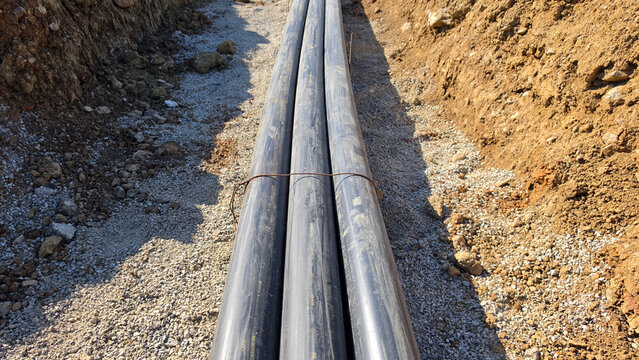 High-angle perspective of a bundled plastic utility conduit run inside a gravel-lined dirt trench