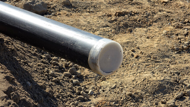High-density polyethylene utility pipe with protective white plastic end cap on a dirt construction site