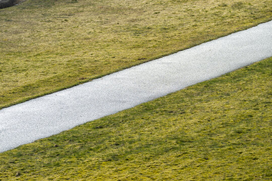 Minimalist diagonal gravel path cutting through muted grassy field landscape.