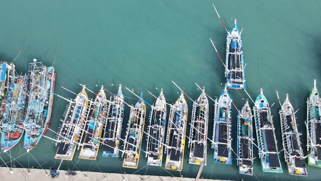 Aerial view of colorful fishing boats moored in orderly rows along the concrete pier in the harbor of Bakauheni, Lampung, Indonesia.