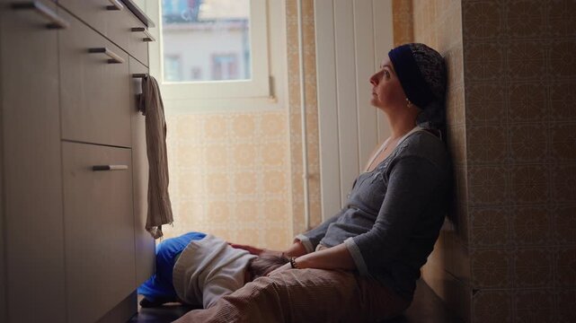 Pensive mother resting on kitchen floor beside toddler, quiet parenting moment expressing reflection, emotional presence, attachment and authentic family life at home