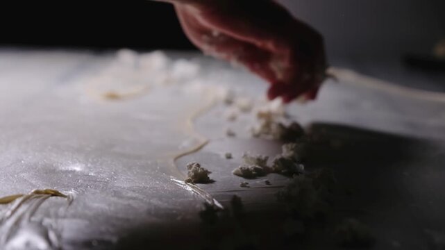 Close-up footage of cheese filling being sprinkled over thin yufka dough during b&ouml;rek preparation, showing handmade Turkish pastry technique, fresh ingredients and traditional kitchen work.