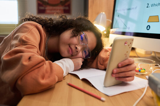 Asian teenage girl resting on desk while holding smartphone during online study at home, showing screen distraction and digital learning fatigue. Useful for education burnout campaigns