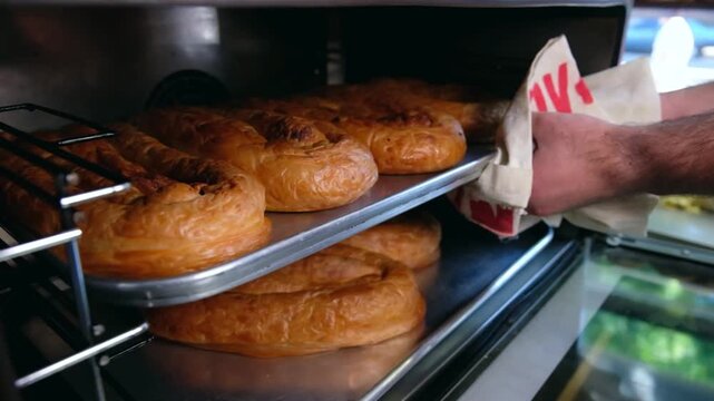 Close-up footage of freshly baked b&ouml;rek trays inside a hot oven, showing golden pastry layers, traditional Turkish food preparation, bakery service and restaurant-style baking process.