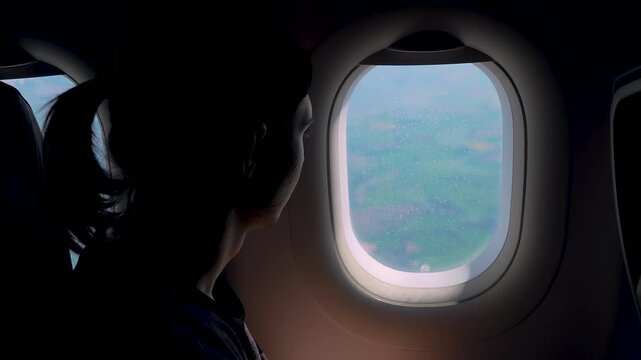 Traveler gazing out airplane porthole at bright sky while plane approaching landing. Male passenger observing changing light and cloud patterns from window seat. Aircraft moving lower through