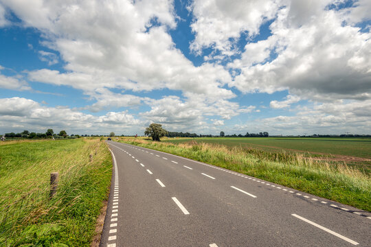 Narrow asphalt road in a rural area in the Dutch province of North Brabant. The photo was taken on a cloudy day.