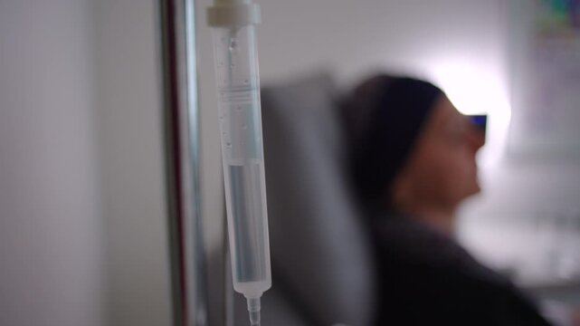 Intravenous drip chamber with falling fluid drops in healthcare setting, medical treatment detail representing patient care, hydration, recovery and wellness