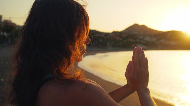 Woman embracing inner peace with clasped hands on a serene beach at golden hour sunset, exuding mindfulness and spiritual connection for wellness and travel.