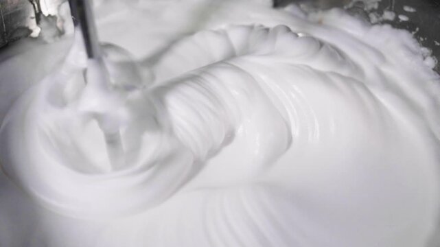 Close-up of a stand mixer whisking egg whites into a stiff, glossy meringue. Food preparation process for desserts like cake or pavlova