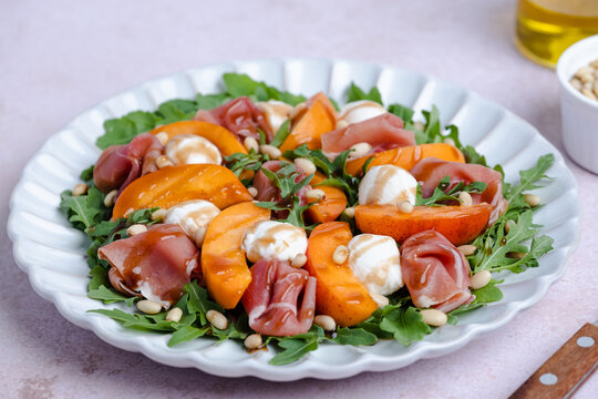 Fresh salad made with arugula, fresh peaches, prosciutto, mini mozzarella cheese, arugula, and toasted pine nuts, drizzled with balsamic glaze. Healthy dining and Mediterranean cuisine concepts.