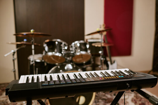 Close up of electronic keyboard standing in music rehearsal studio with drum kit in background, representing band practice and music production use for entertainment marketing