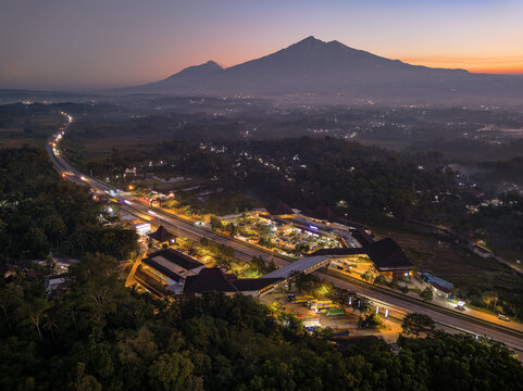 Aerial view of Rest Area Pendopo KM 456 B illuminated at twilight with the Trans Java Toll Road and Mount Merbabu in the background in Pabelan, Central Java, Indonesia.