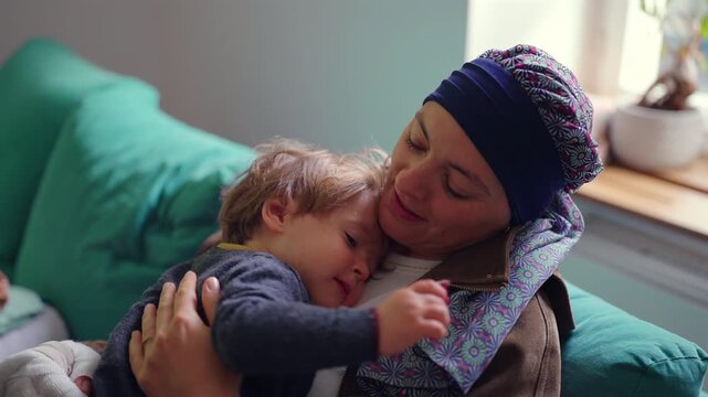 Mother undergoing chemotherapy embracing toddler on sofa at home, cancer treatment journey highlighting resilience, family support, healing and emotional strength