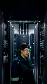 Focused female engineer inspecting server racks with headlamp in dark data center