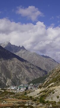 Stunning vertical timelapse landscape view of a high altitude mountain settlement nestled in a deep rocky valley under dramatic moving clouds. (Chitkul Village)