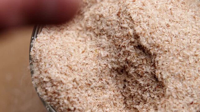 Human hand taking a pinch of organic psyllium husk from a glass container. Flaky texture of the soluble fiber. Keto baking ingredient