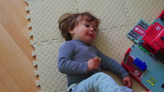 Toddler resting on play mat beside toy vehicles at home, quiet childhood moment highlighting relaxation, comfort, wellbeing and everyday family life