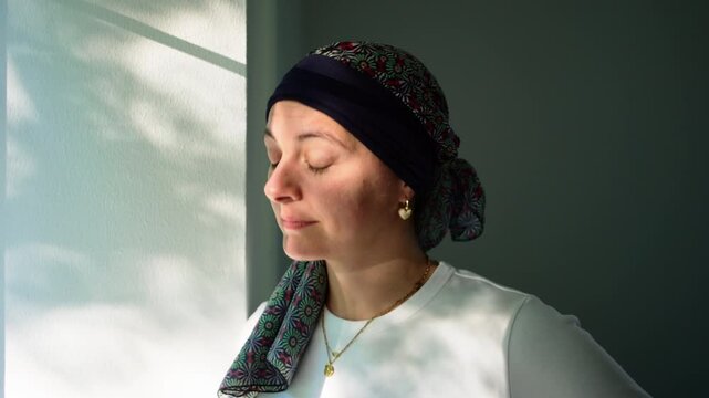 Woman in cancer recovery looking through window at home, reflective moment highlighting resilience, hope, healing, strength and optimism during recovery journey
