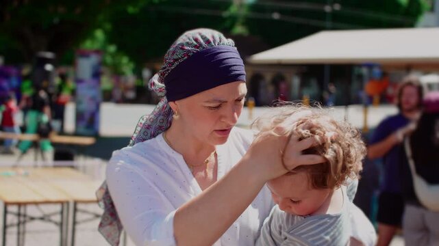 Mother holding toddler child during outdoor community gathering, affectionate parent child moment highlighting attachment, security, care and family connection