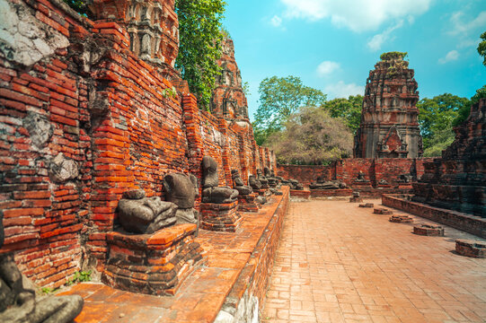 Ancient headless Buddha statues lining the red brick wall at Wat Mahathat in Ayutthaya, Thailand.