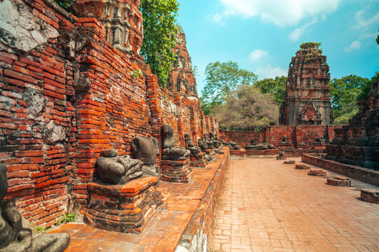 Ancient headless Buddha statues lining the red brick wall at Wat Mahathat in Ayutthaya, Thailand.