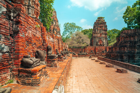 Ancient headless Buddha statues lining the red brick wall at Wat Mahathat in Ayutthaya, Thailand.