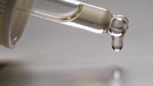 Making clear dropper releasing droplet as liquid flowing at lab mat, with cap reflection by gravity