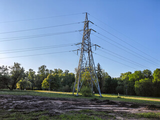 Obraz premium High voltage power line pylon in green park landscape with muddy tracks