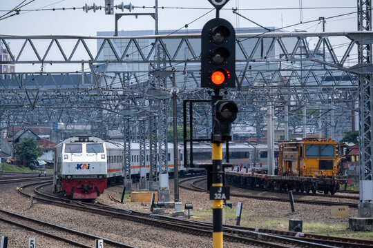 Jakarta, Indonesia - May 28, 2026: A KAI long-distance passenger train led by a CC206 diesel-electric locomotive passing a yellow ballast tamping machine near a railway signal at Jatinegara Station.